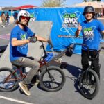 Two BMX riders posing with bikes in front of Go Big BMX Air Show banner promoting stunts and anti-bullying messages