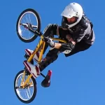 BMX rider in helmet performing mid-air trick during freestyle session, highlighting safety gear